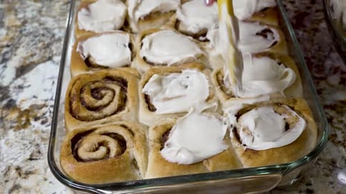 Dabbing frosting or icing on freshly baked cinnamon rolls - isolated close up