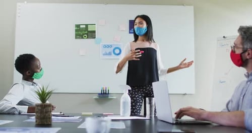 Asian woman wearing face mask giving presentation to her colleagues in meeting room at modern office