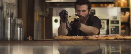 Italian chef grating parmesan cheese over special al taglio pizza with roast beef topping.