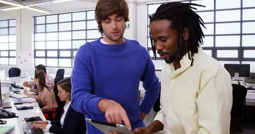 Two Young Adults Collaborate Over Tablet in Office