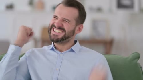 Man Celebrating Success While Sitting on Sofa