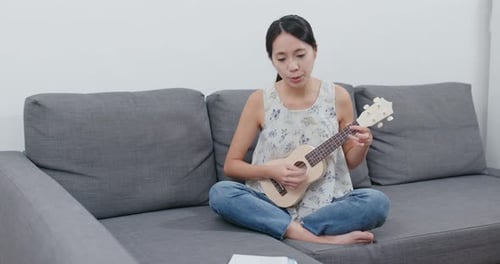 Woman play a song with ukulele at home