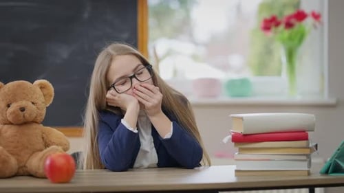 Tired Schoolgirl Yawning Taking a Nap Putting Head on Desk in Classroom