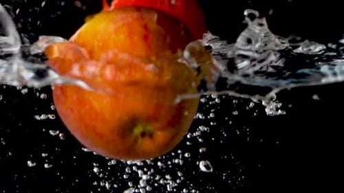 Zwei rote Äpfel fallen in Zeitlupe vor einem schwarzen Hintergrund ins Wasser.