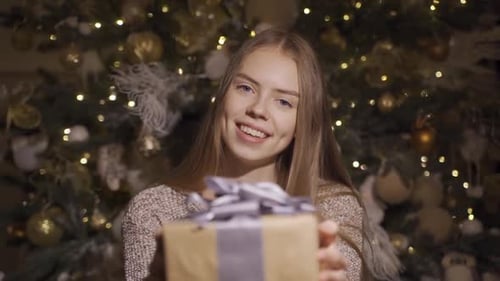 Woman Offers Gift in Front of Christmas Tree