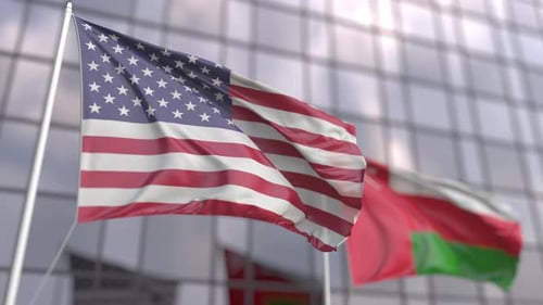 Waving Flags of the USA and Oman in Front of a Skyscraper