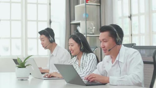 Three Asian Call Centre Agents Speaking To Customers On The Call At The Office