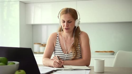 Woman with Laptop Writing in Notebook at Home