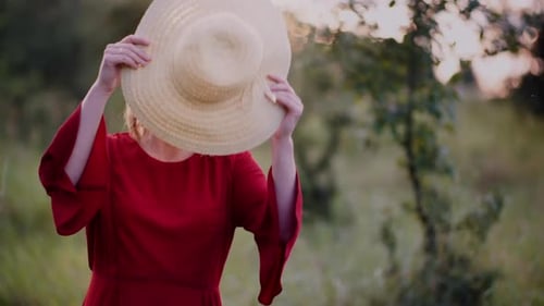 Woman Puts on Hat in Field at Sunset