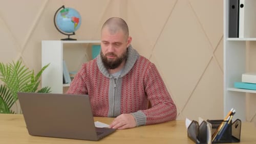Man on Video Call Taking Notes at Desk