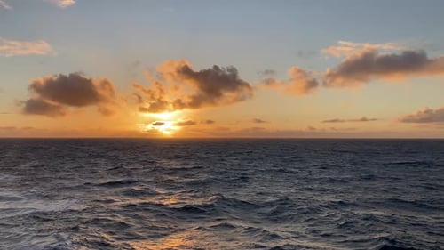 Bold and colorful sunset sky and clouds over ocean waves, motion background