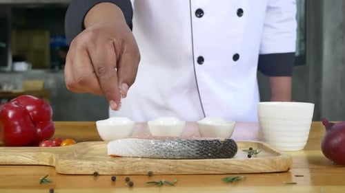 chef or cook seasoning fresh chunk of deli piece of beef with sea salt and grounded spicy peppers.