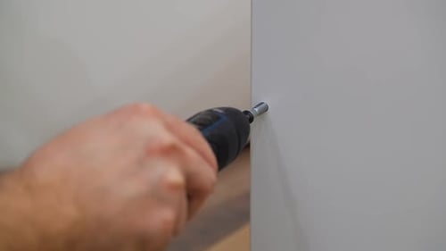 Hand uses drill to screw in furniture screw