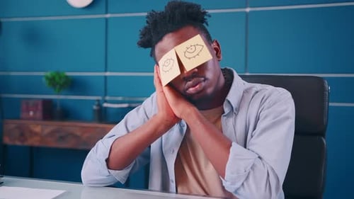 Man 'Sleeping' at Desk with Sticky Notes on Eyes