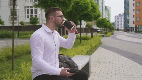 Man Drinking Coffee and Using Smartphone Outdoors