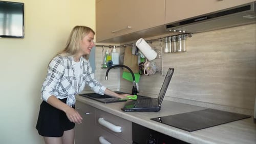 Woman Cleaning Kitchen While Looking at Laptop