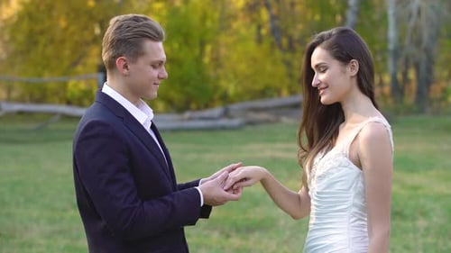 Bräutigam legt schönen Ring an den Finger seiner Braut in sonnigen Strahlen im Autumn Park