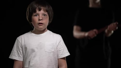 Frightened Caucasian Boy with Scared Facial Expression Looking at Camera As Unrecognizable Mother