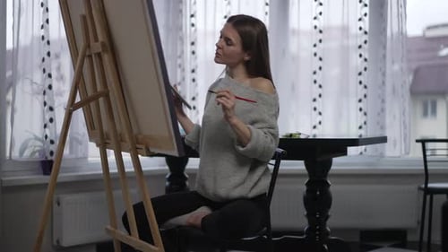 Woman Painting on Canvas in Brightly Lit Room