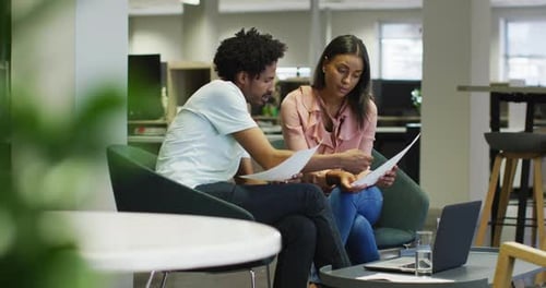 Video of focused diverse businesswoman and businessman with papers talking