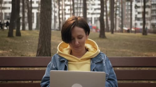 Woman with laptop working remotely in park.