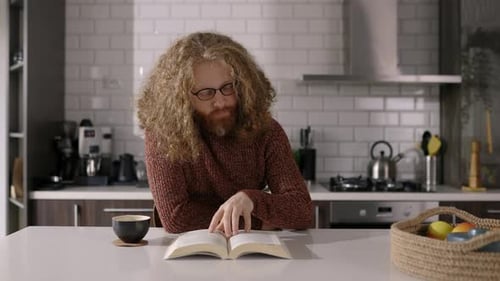 Man Reads Book in Kitchen with Coffee