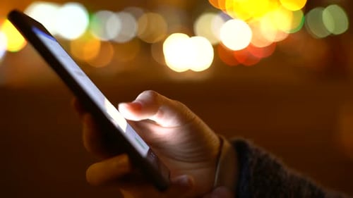 Hand Scrolls Smartphone Screen at Night in City