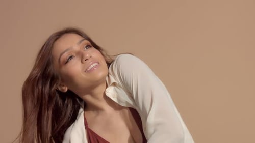 Young Brunette Woman Dancing in Studio on Beige Background