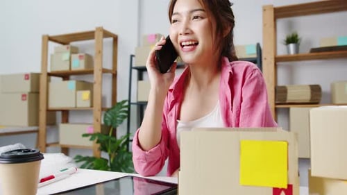 Young Woman on Cell Phone Packs Box at Desk