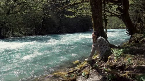 Junge Frau sitzt am Ufer in der Nähe des Swift River und schaut auf das Wasser