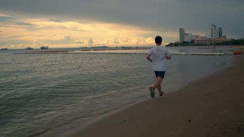 Long shot Asian sportsman running on the beach during a beautiful sunset in summer.