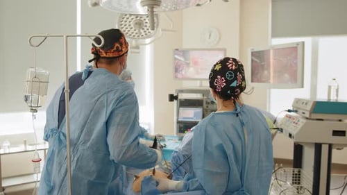Back View of Surgeons Team Looks at Monitors While Preforming Operation in