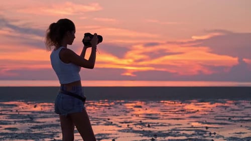 Femme prenant des photos du coucher de soleil sur la plage