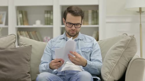 Frustrated Man Reads Documents on Couch at Home