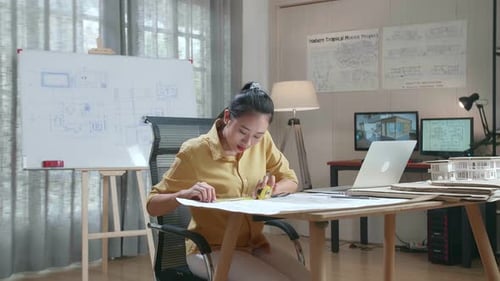 Asian Woman Engineer With A Laptop Measuring Blueprint At The Office