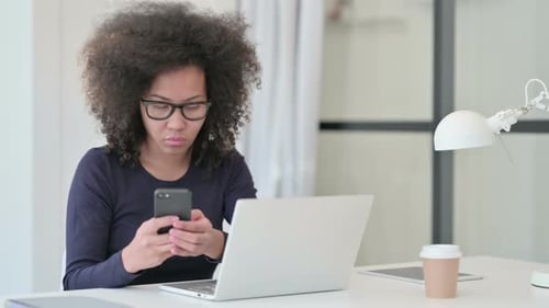 Young Woman Using Phone at Desk with Laptop