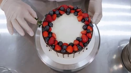 A Pastry Chef Decorates a Cake with Berries and Mint Leaves in a Pastry Shop