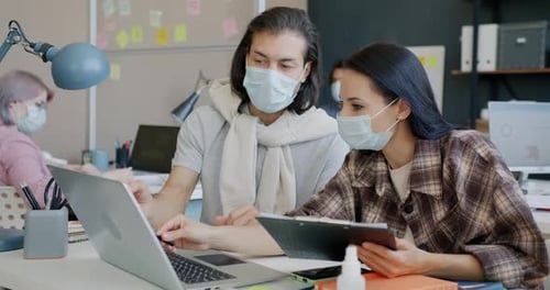 Man and Woman Colleagues Working with Laptop and Talking Wearing Face Masks in Office
