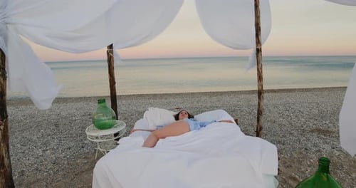 Young girl sleeps in a canopy bed at sunset on the beach near the ocean