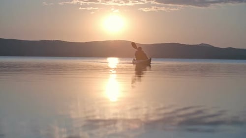 Man kayaking at sunset in tranquil ocean waters
