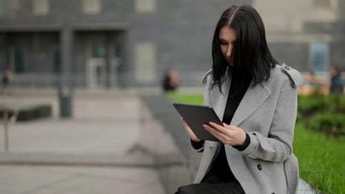 Elegant Woman is Working with Tablet on Street Sitting in Park in Autumn