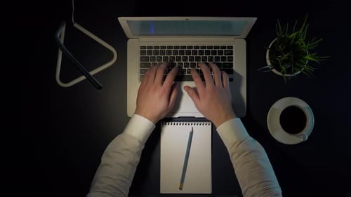 Männlicher Geschäftsmann im weißen Hemd sitzt abends am Tisch, arbeitet am Laptop und trinkt