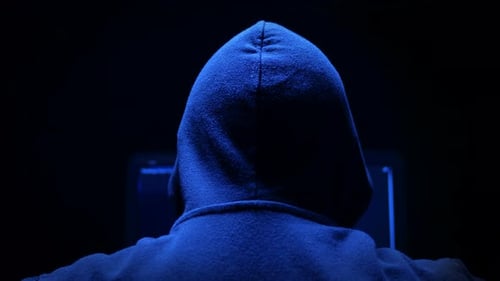 Hacker mit Kapuze arbeitet im Dunkeln an einem Computer
