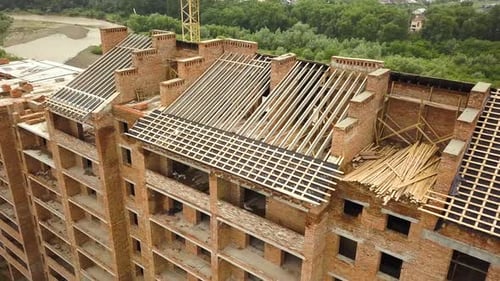 Aerial view of unfinished brick apartment building with wooden roof structure under construction.
