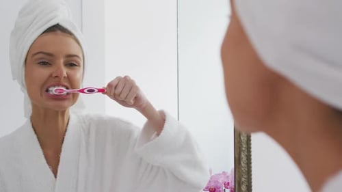 Woman Brushing Teeth in Bathroom Mirror