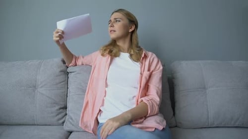 Woman Fanning Herself on Couch with Paper