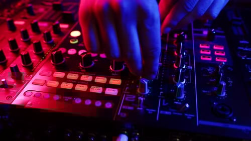 Closeup of hands of DJ tuning sound by turning knobs and pressing buttons on mixing console in club