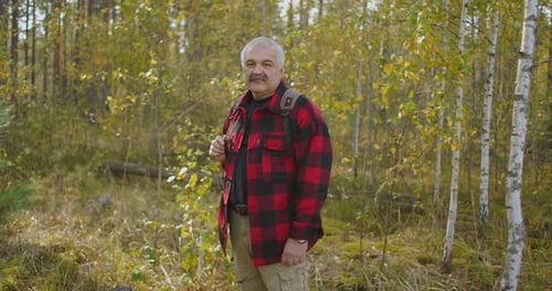 Cheerful Middle-aged Man Is Standing in Autumn Forest with Yellowed Trees at Daytime, Smiling To