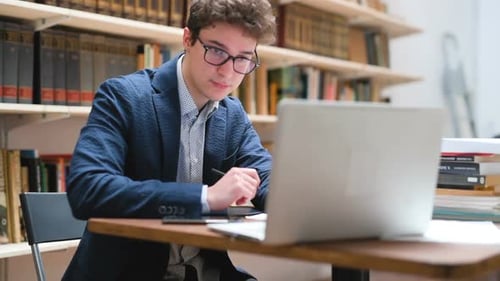 Students studying over desktop computers while sitting at table in library using digital tablet