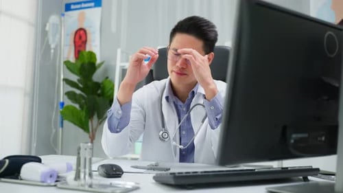 Stressed and overworked Asian male doctor sitting on table in hospital.